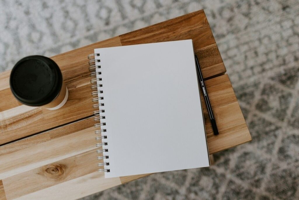 Offenes blankes Notizbuch mit Stift und Kaffee auf einem Holztisch